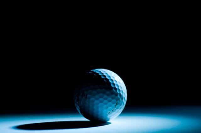 blue golf ball sitting in the dark being hit by a beam of light