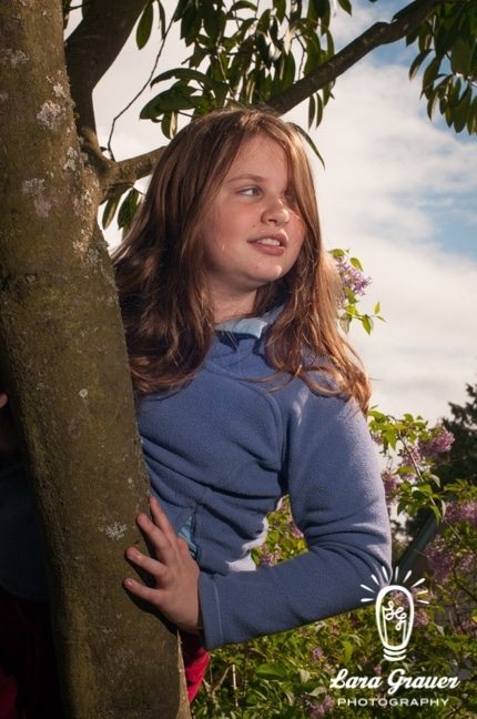 brown haired teenage girl standing behind a tree