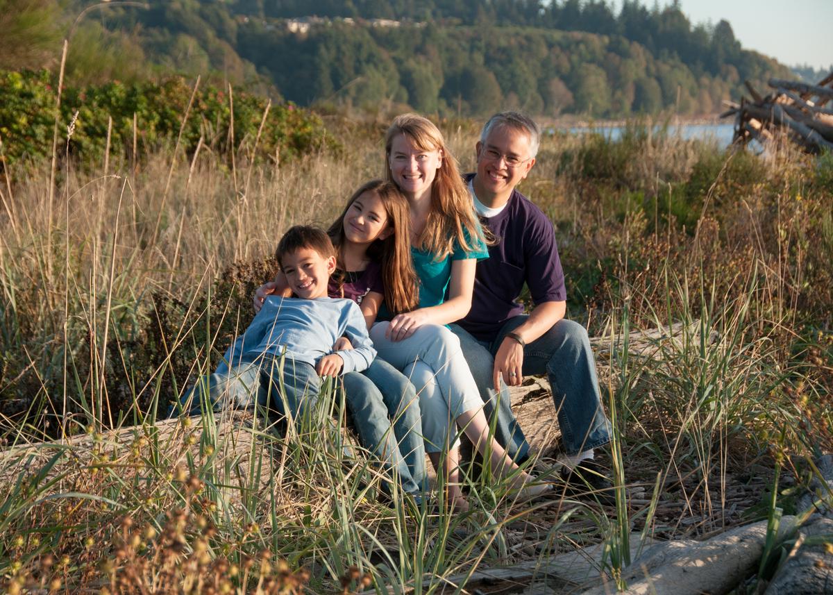 mom, dad, daughter, and son sitting a log near a beach waterfront
