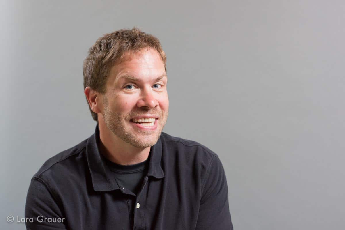 man in a black polo shirt looking into the camera while smiling.