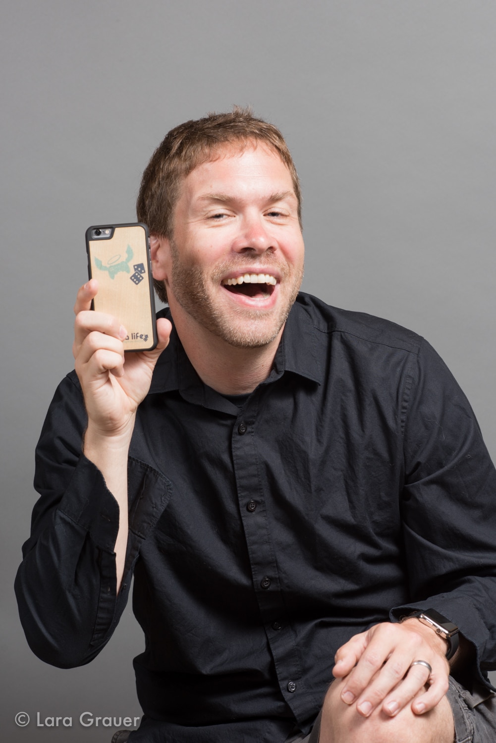 photo of a man in a black button down shirt holding a phone with a happy expression.