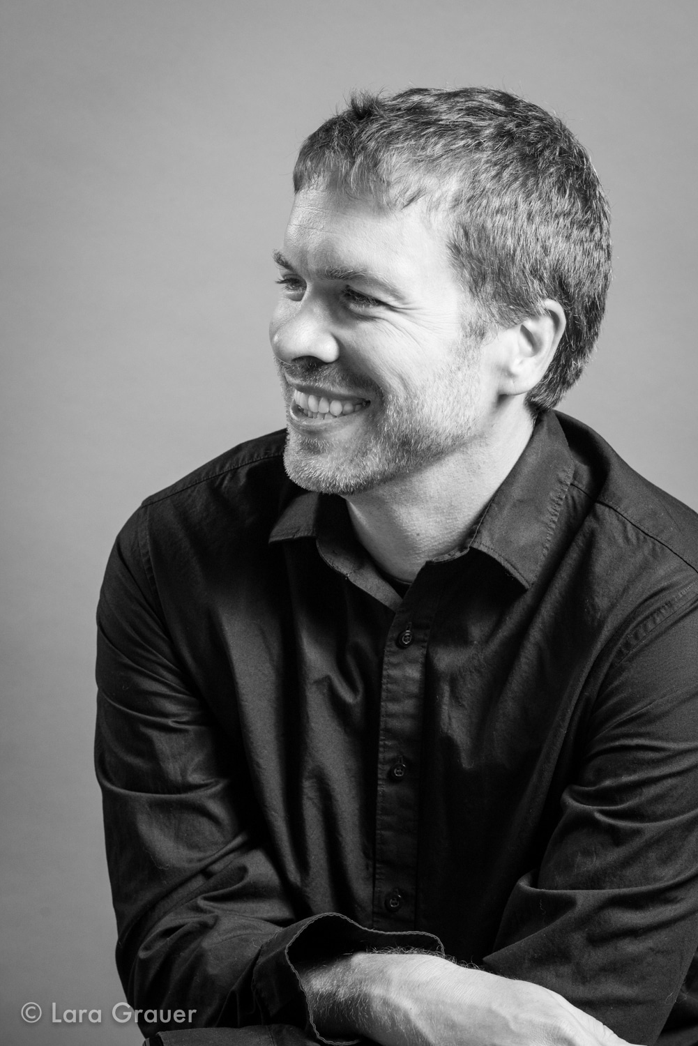 black and white photo of a man in a buttoned down shirt smiling.