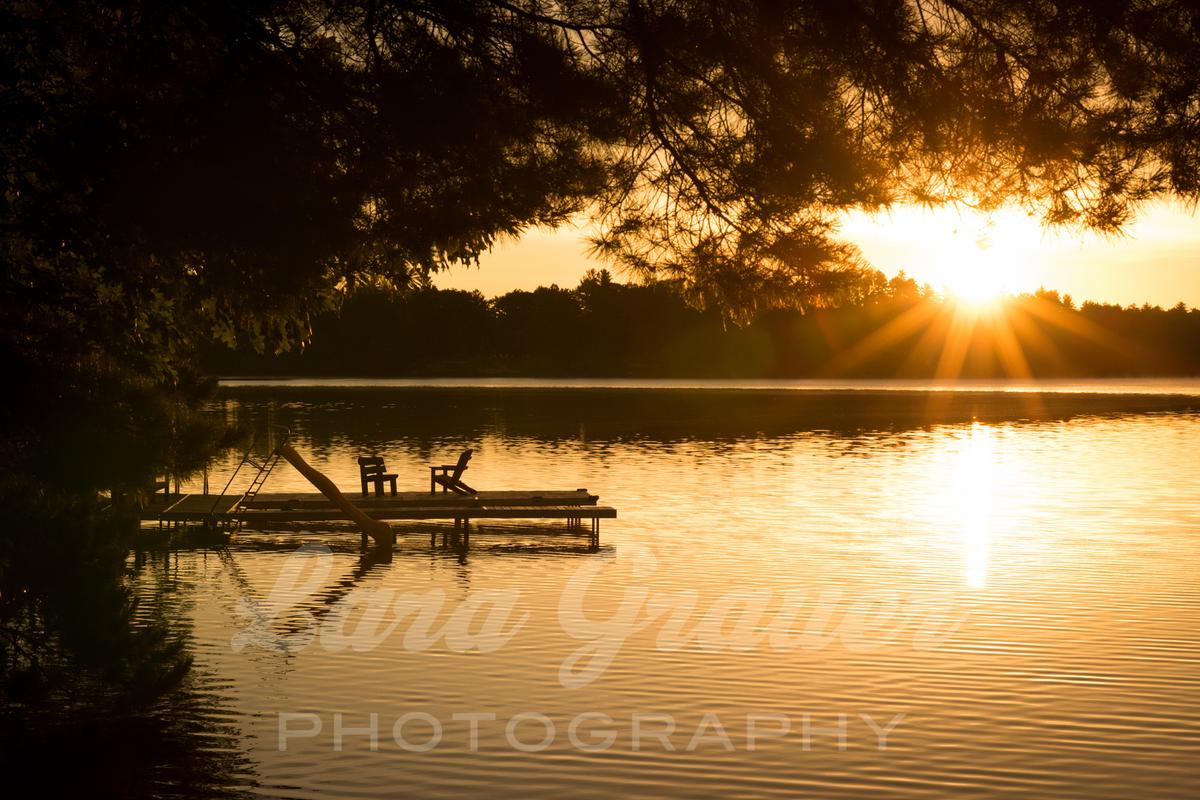 sunset photo of a dock on a lake with two chairs and a slide