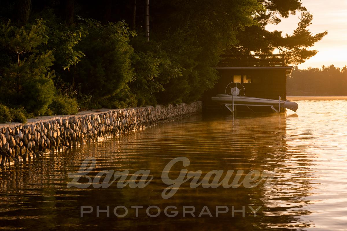 stone wall and small boat on the side of a lake with the lara grauer photography logo