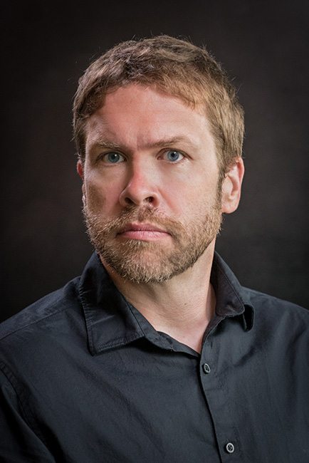 headshot of a man with short hair and short beard with dark gray button-up shirt.