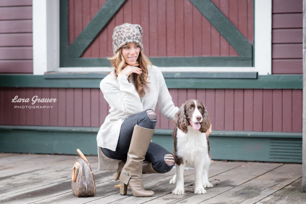 women in cheetah print hat kneeling and posing with her brown bag and white and brown bag dog.