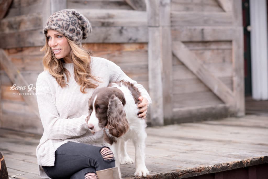 women in cheetah print hat posing with her brown and white dog.