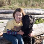 young girl with yellow shirt outdoors with her large black dog.