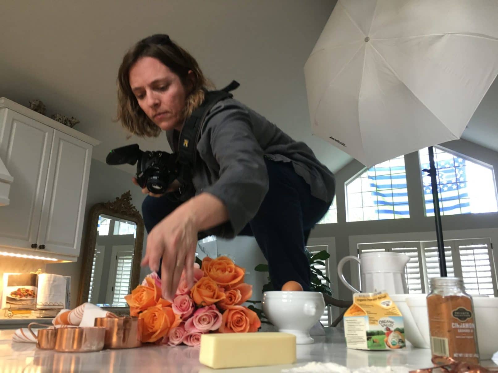 women with dslr camera standing on top of a table positioning food.