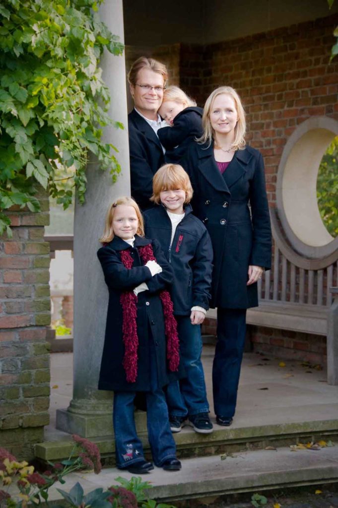 family of five with two daughters and a son posing on their front porch for a family photo.