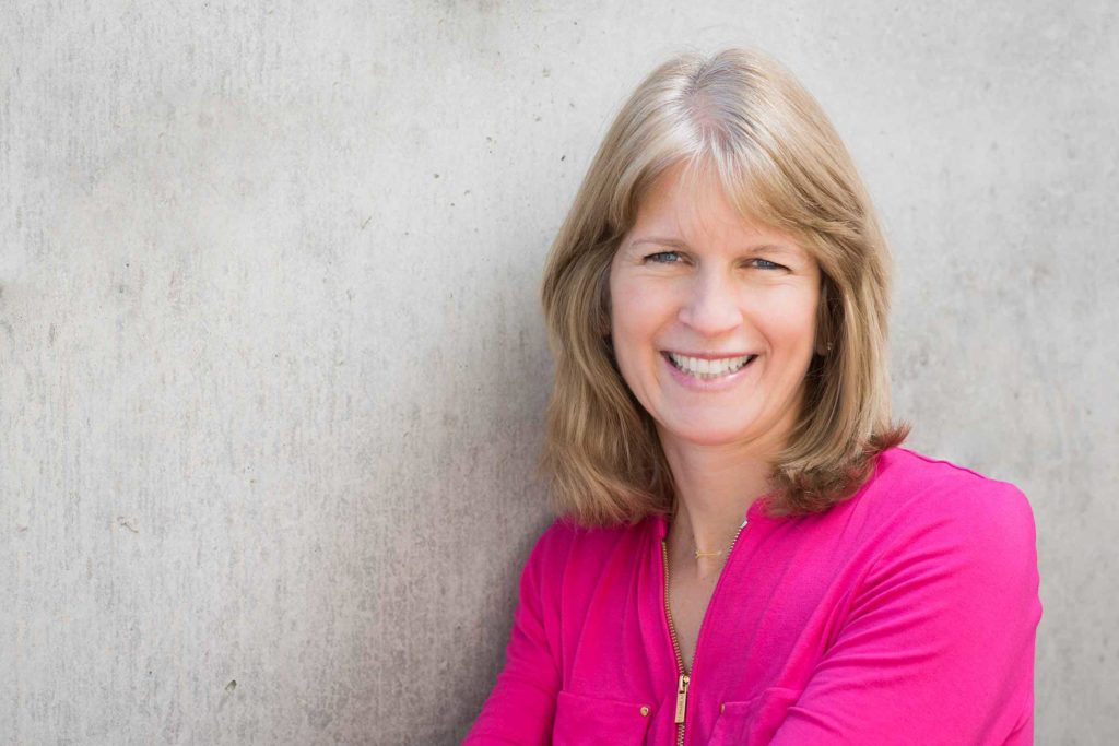 blonde middle aged woman wearing hot pink top smiling towards the camera.