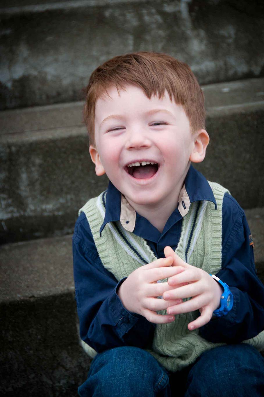 portrait of a laughing young boy in a blue and green sweater.