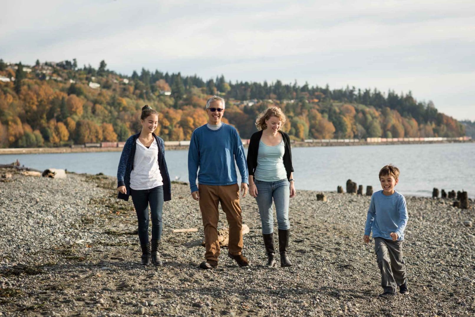 photo of a family walking on rocks alongside a water front with trees in background.