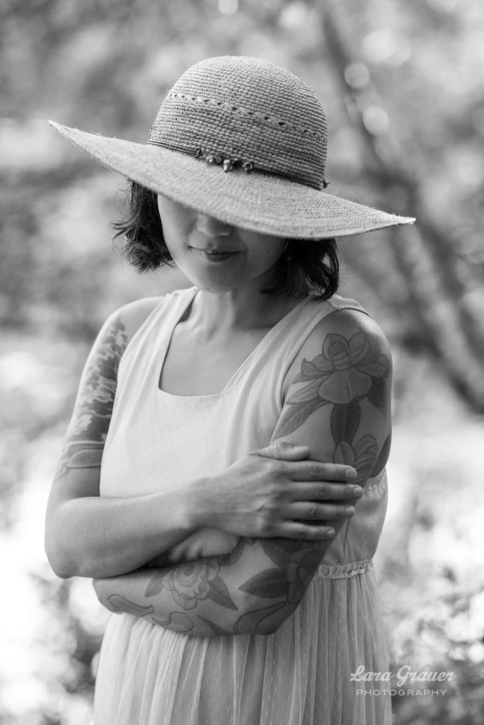 black and white photo of a women with tattoos and a hat covering her eyes.