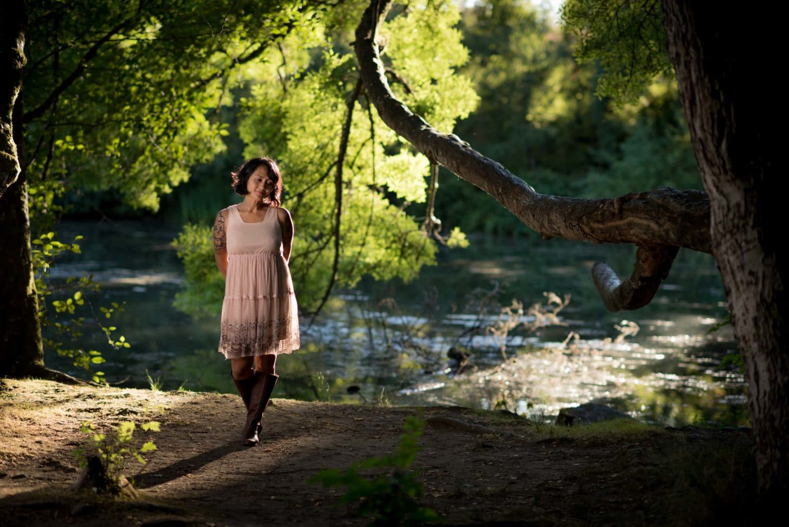photo of women in light pink dress and boots posing by a river.