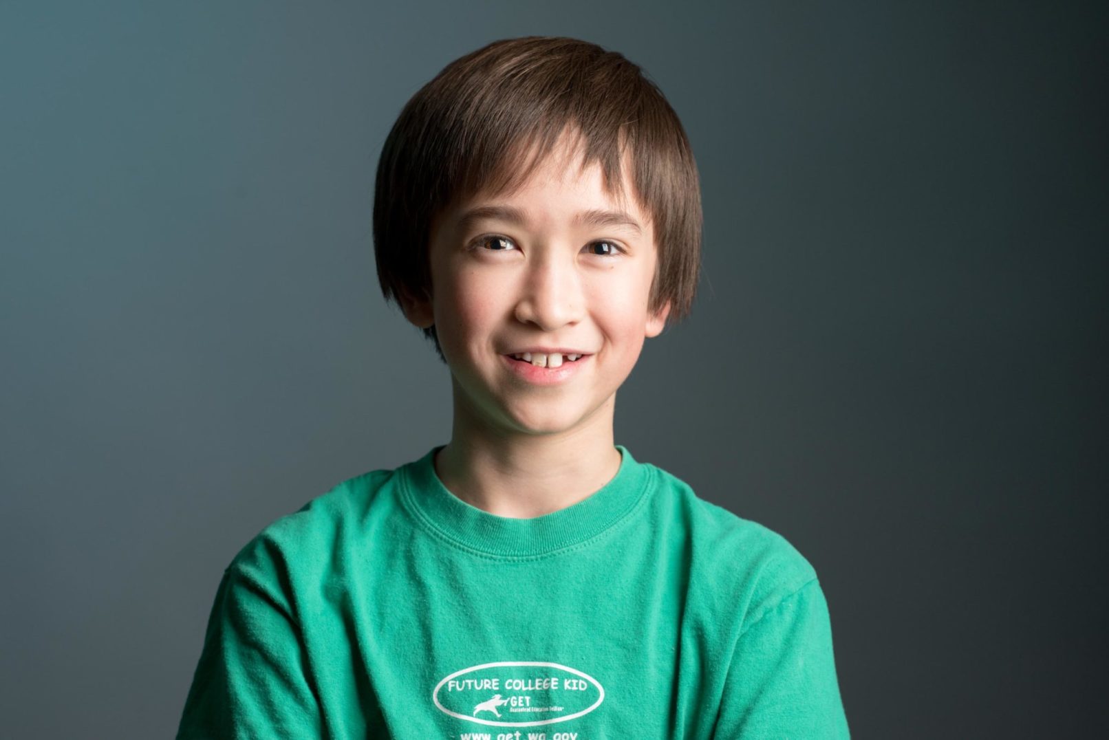 headshot portrait of a young boy wearing a green shirt.