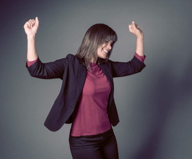 woman wearing red and dark red cheering with her hands above her head.