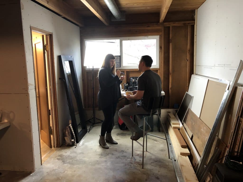 women doing makeup on a male client in an unfinished photography studio.