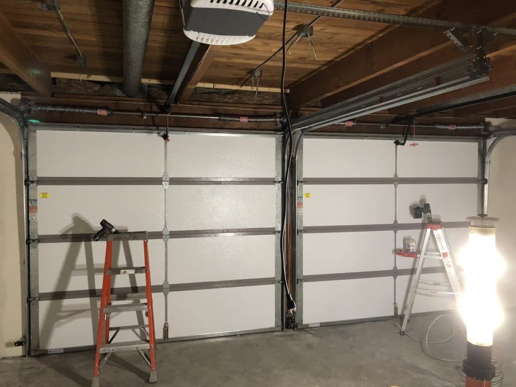 two white garage doors with ladders in front of them.