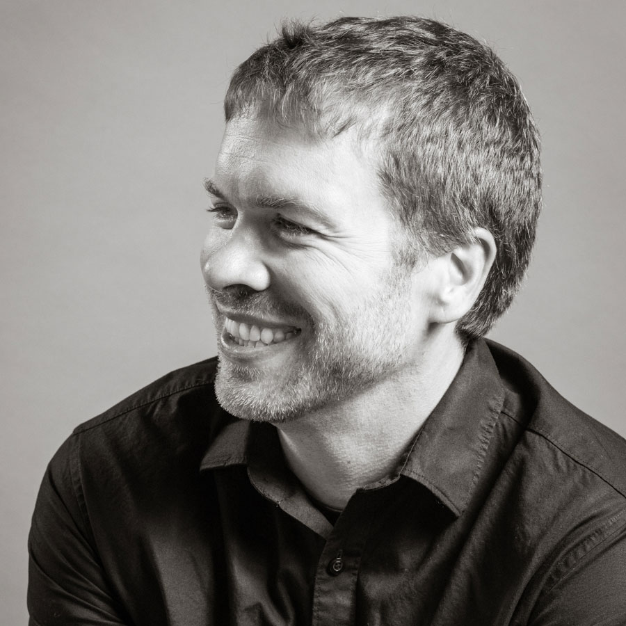 black and white headshot photo of a man laughing and looking to the left.