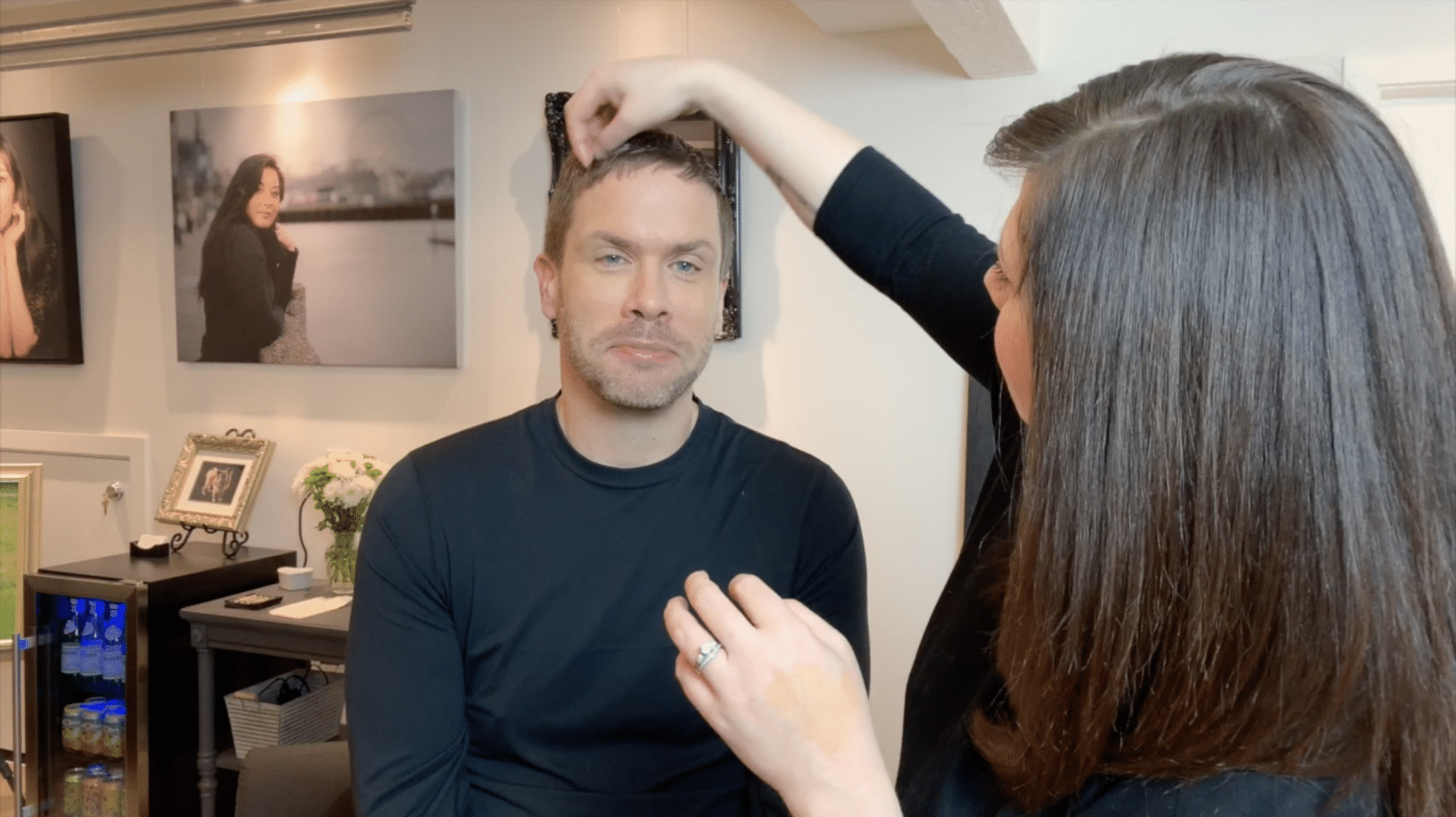 woman with brown hair doing make up for a man with short hair and black shirt