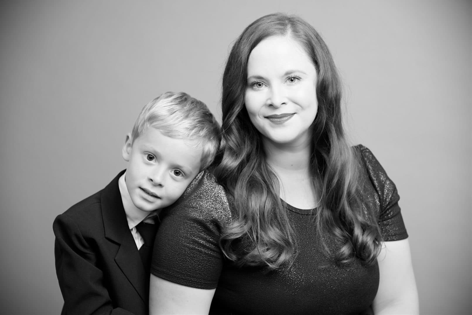 black and white picture of a son wearing a suit leaning his head on mothers shoulder.