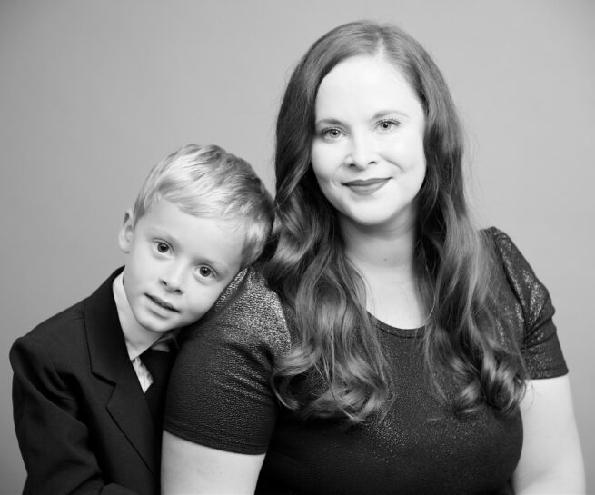 black and white picture of a son wearing a suit leaning his head on mothers shoulder.