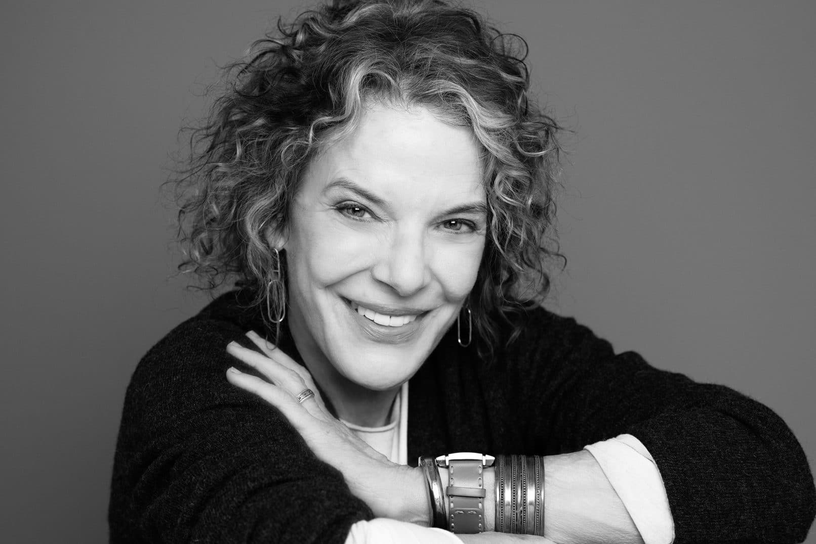black and white photo of a middle aged woman with curly hair looking at the camera.