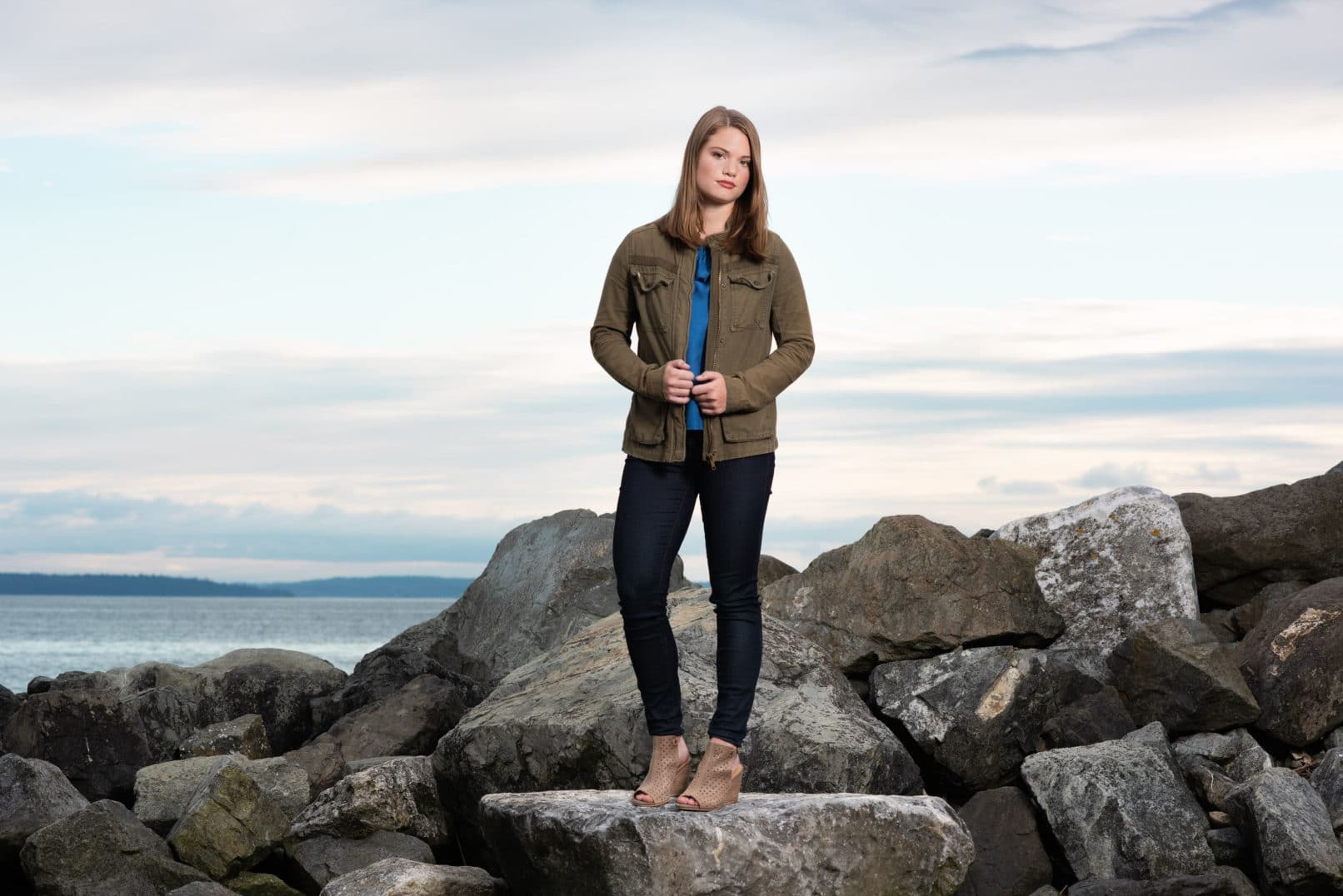 young girl in black pants and navy green jacket standing on rocks