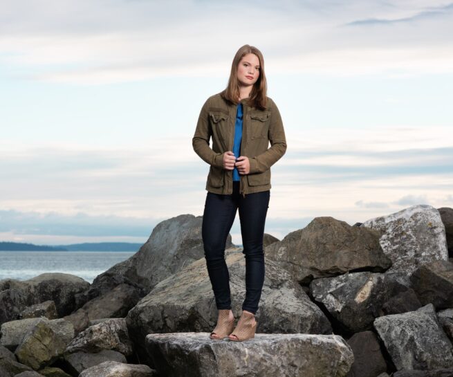 young girl in black pants and navy green jacket standing on rocks