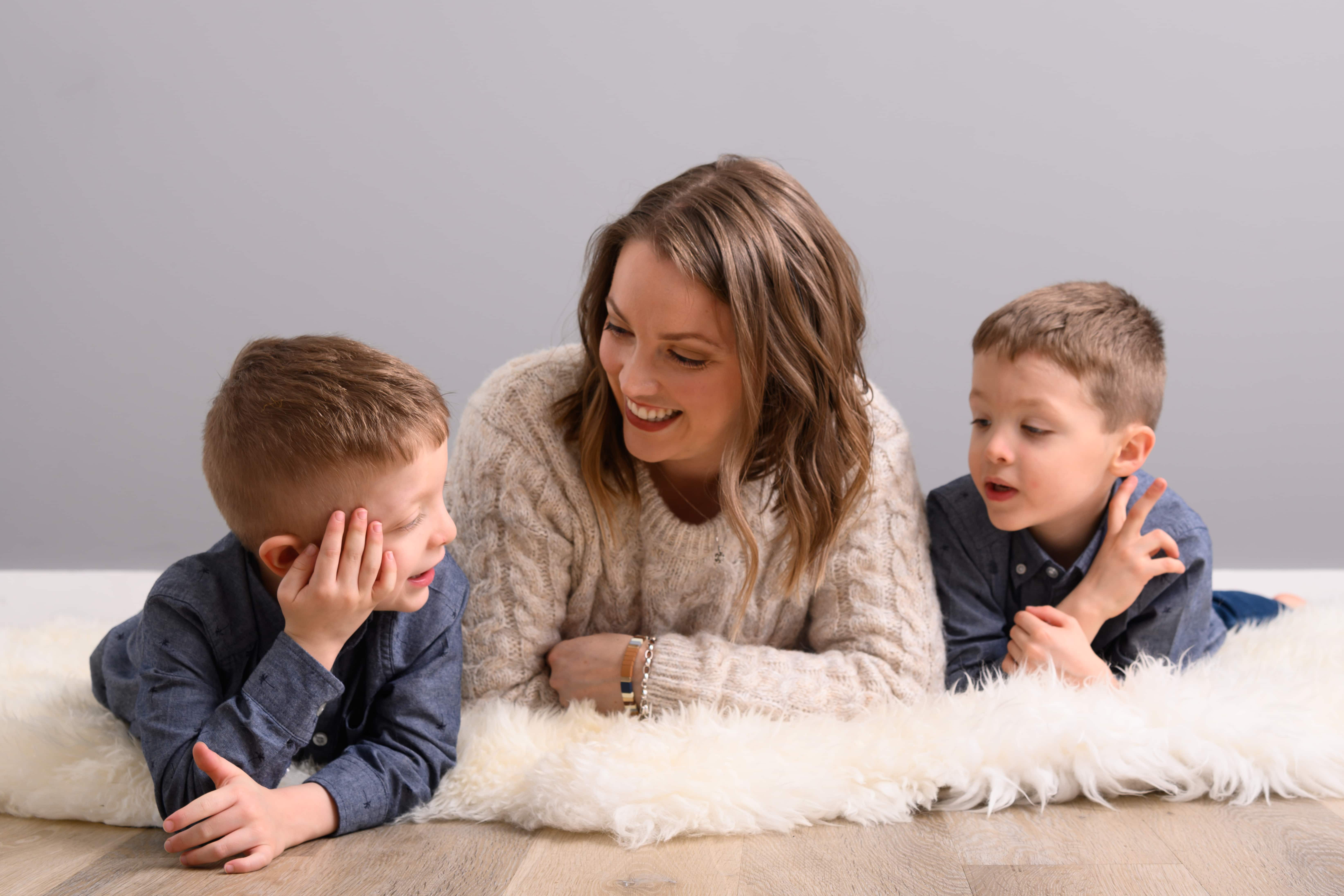 mother with her twin sons laying on the floor on a furry carpet.