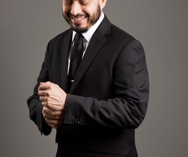 man in black suit and black tied looking at and adjusting his suit cuffs