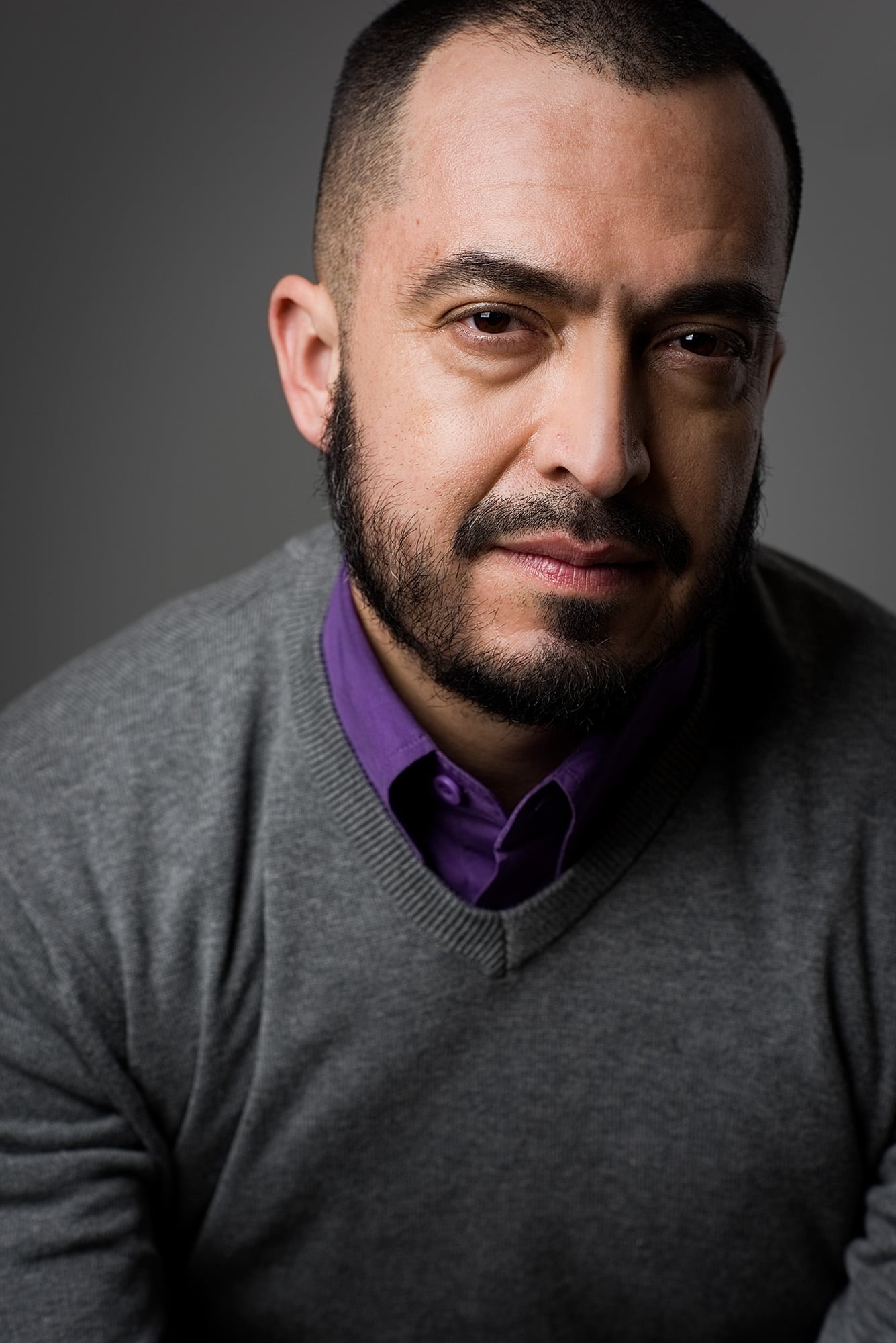 professional headshot of a man in grey sweater and purple undershirt