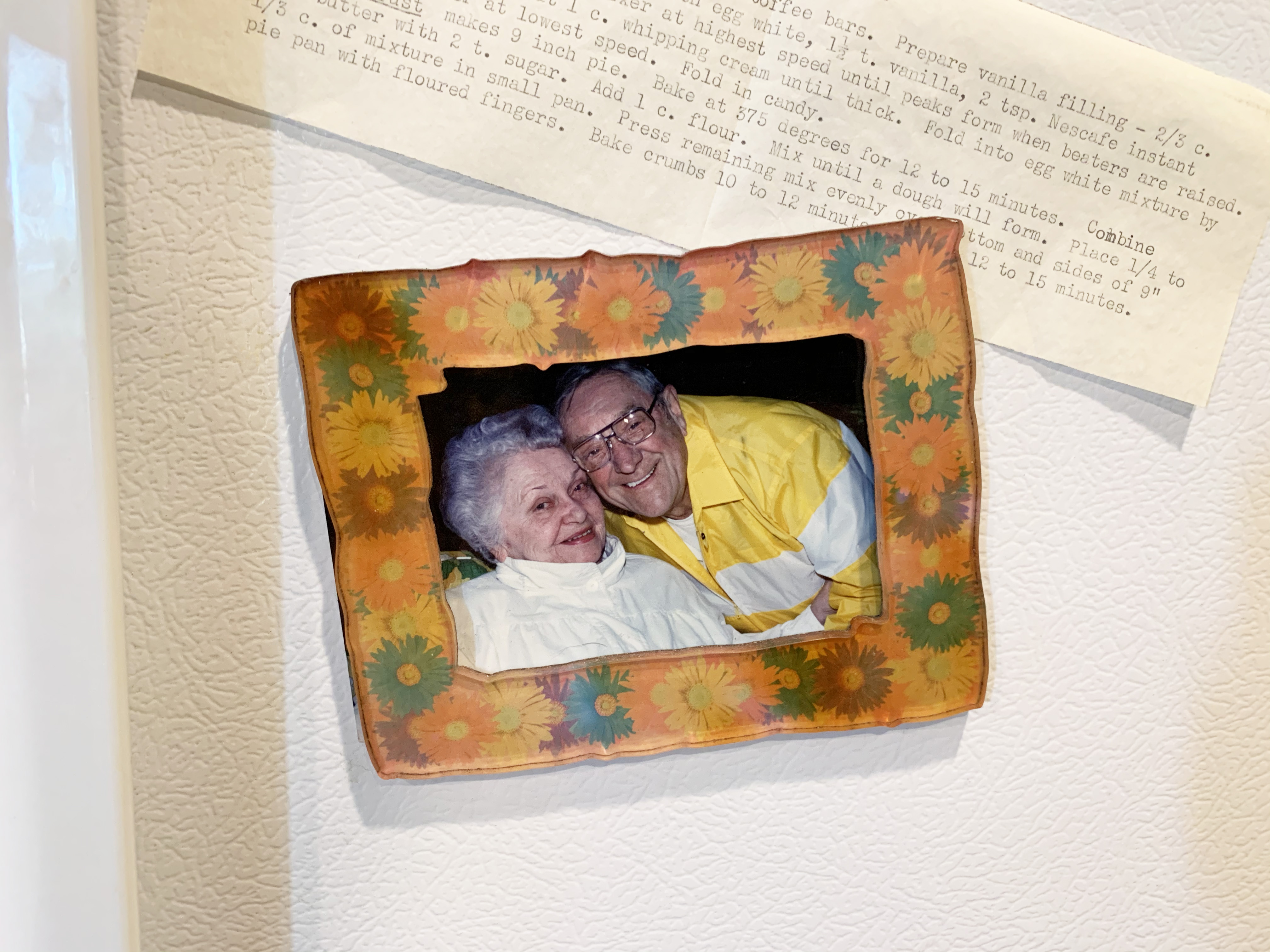 a printed image of grandparents in an orange frame on a fridge with a printed recipe under it