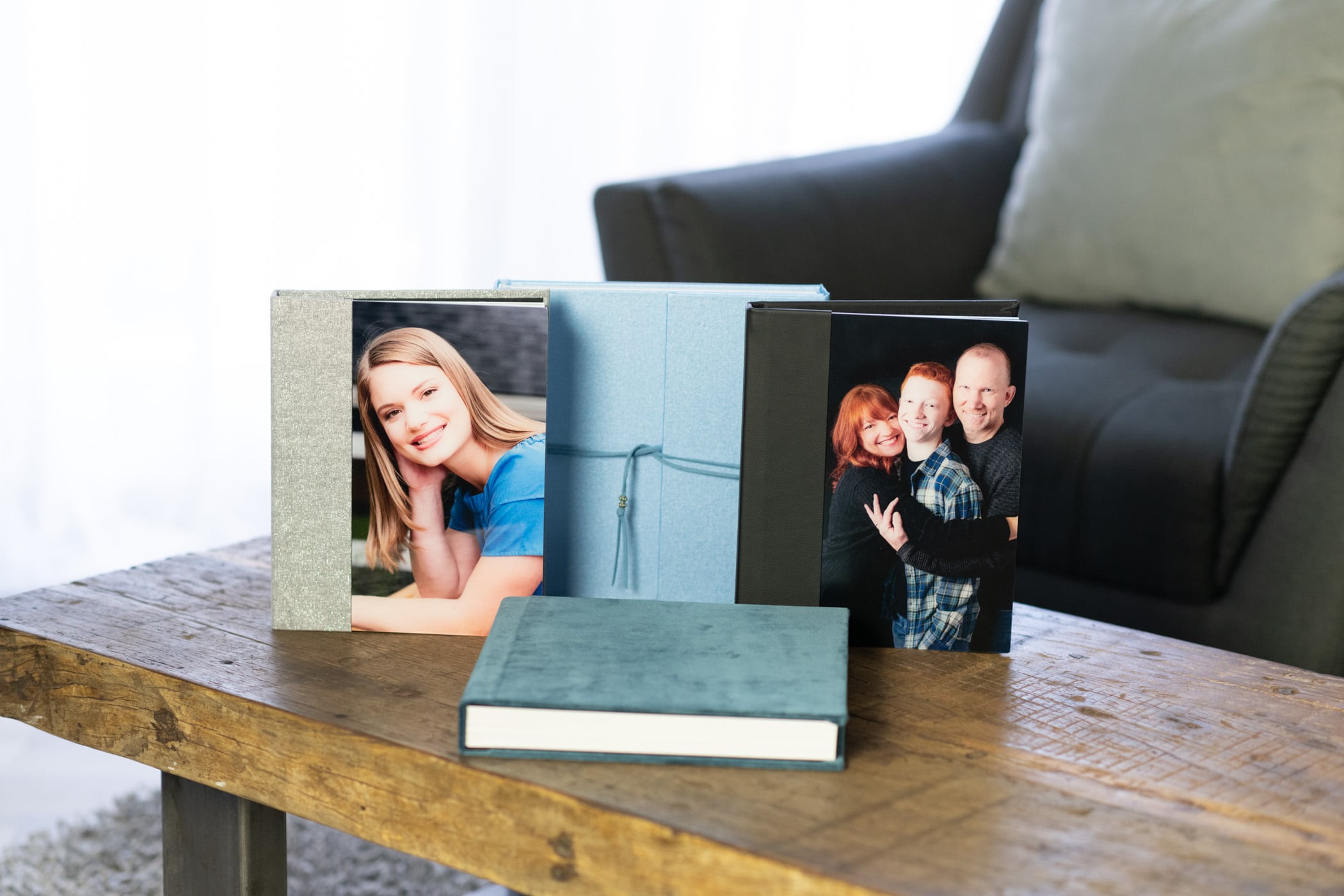 photo albums displayed on a wooden coffee table top with a cusioned chair and whited out background.