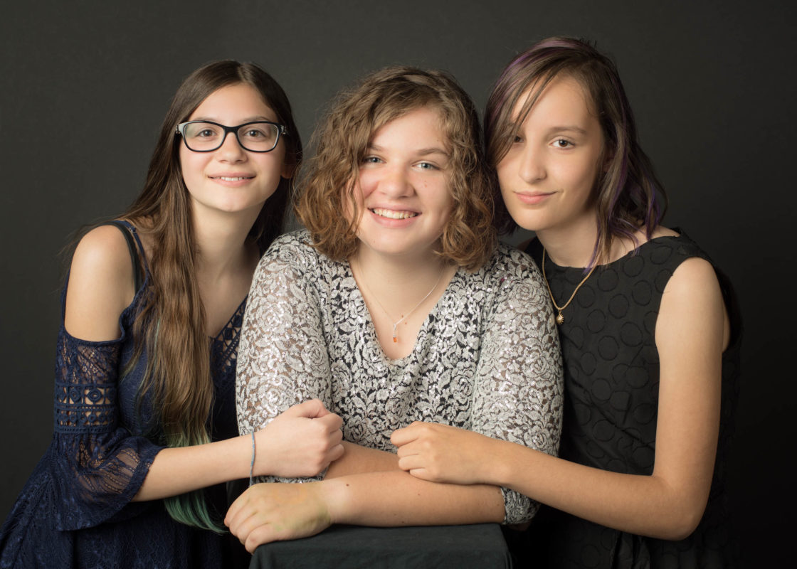 three ladies, one mother in middle with each of two daughters holding their mothers arm.