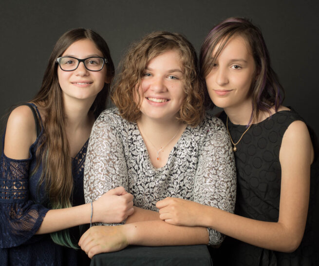 three ladies, one mother in middle with each of two daughters holding their mothers arm.