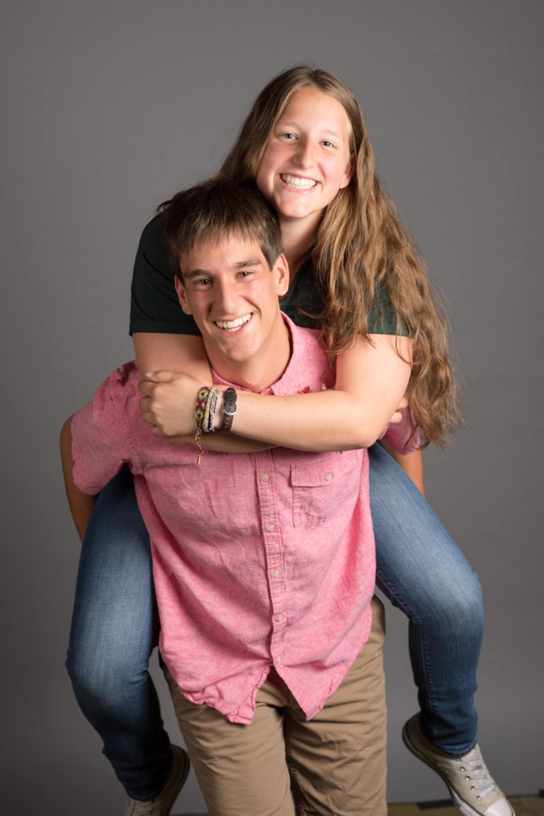 twin sister and brother casually dressed with sister on the back of brother.