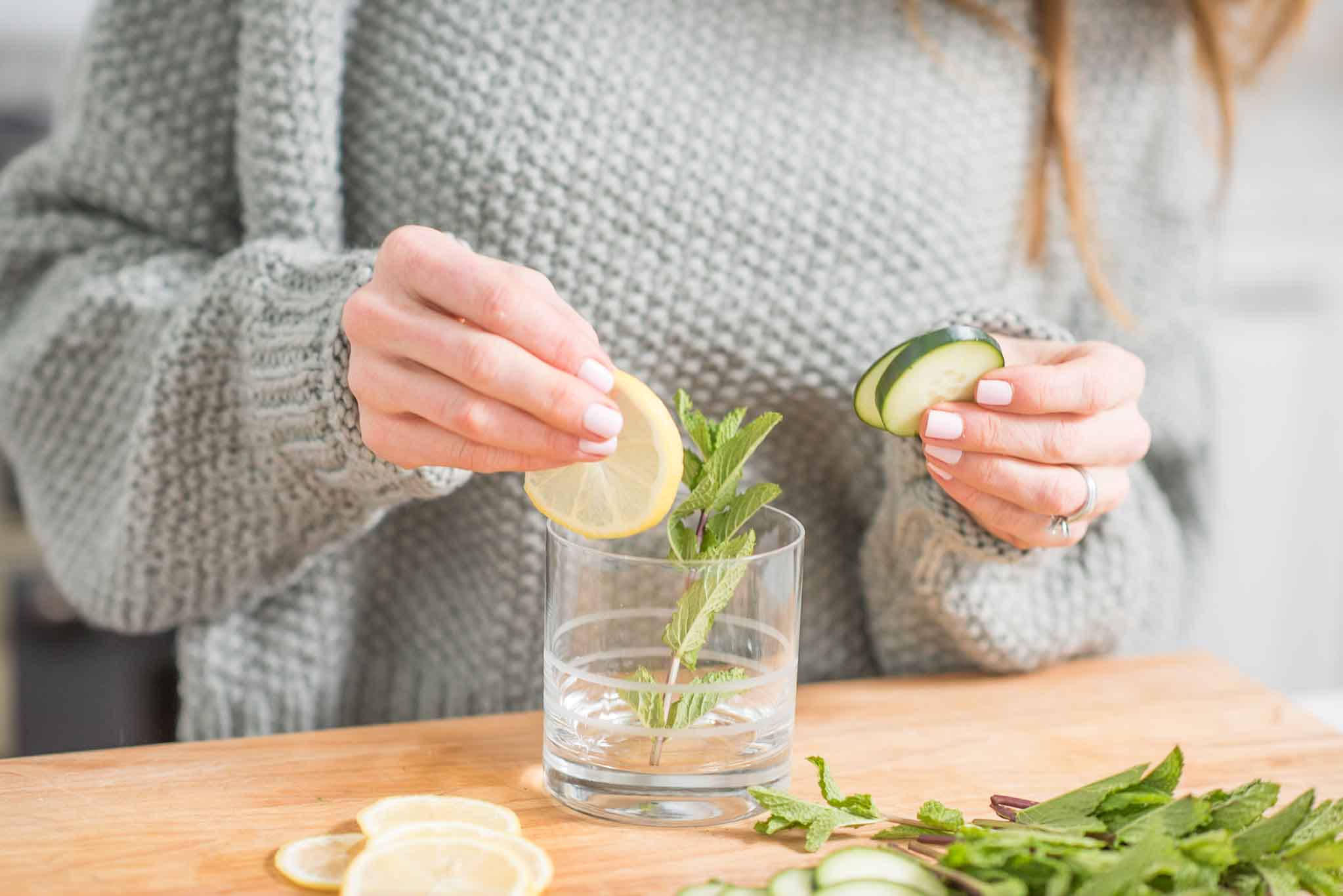 women making a beverage with fresh mint leaves, sliced lemon and cucumber. A partial view of women with close up of torso.