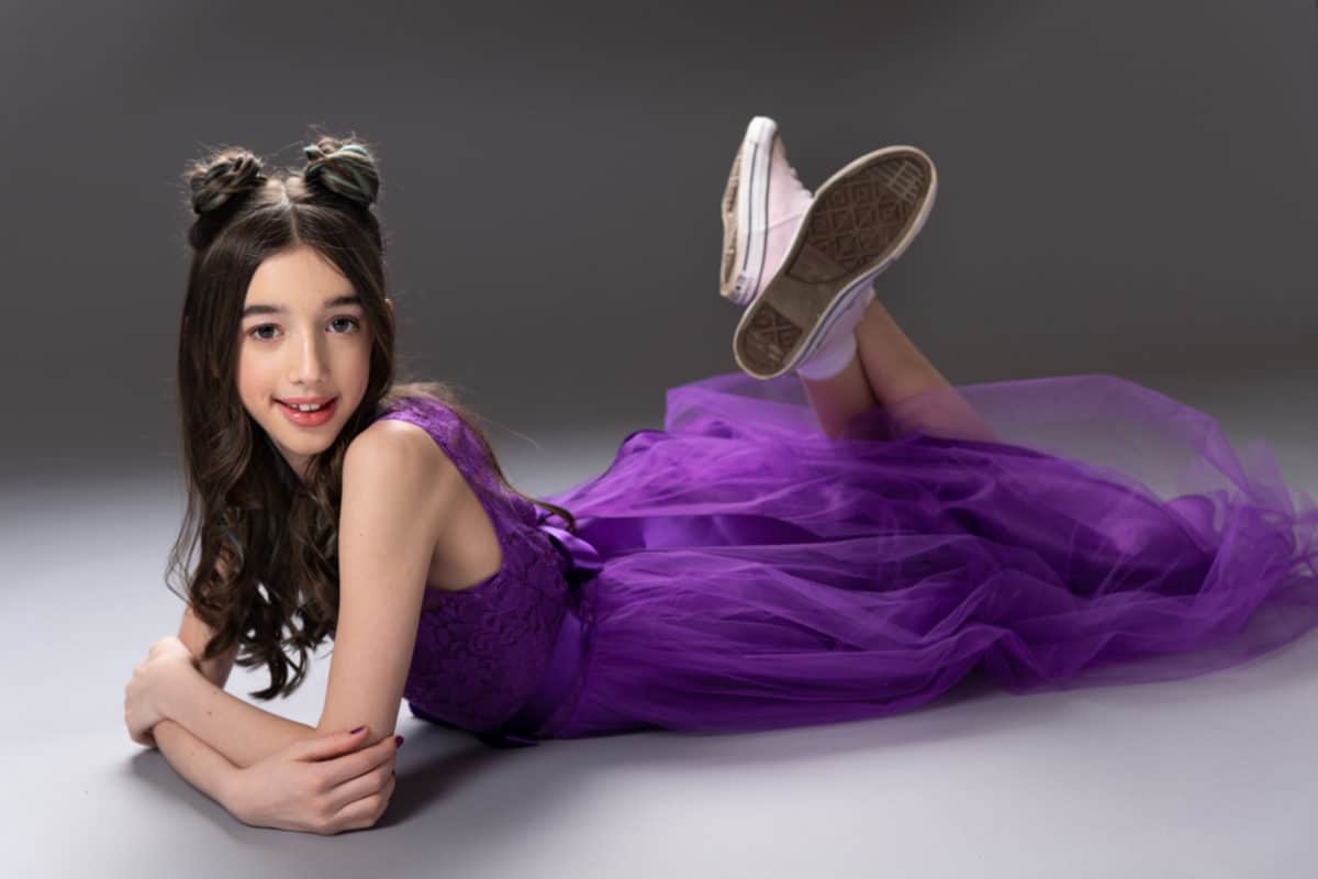 girl with buns in her hair laying on the floor wearing a purple gown and pink sneakers