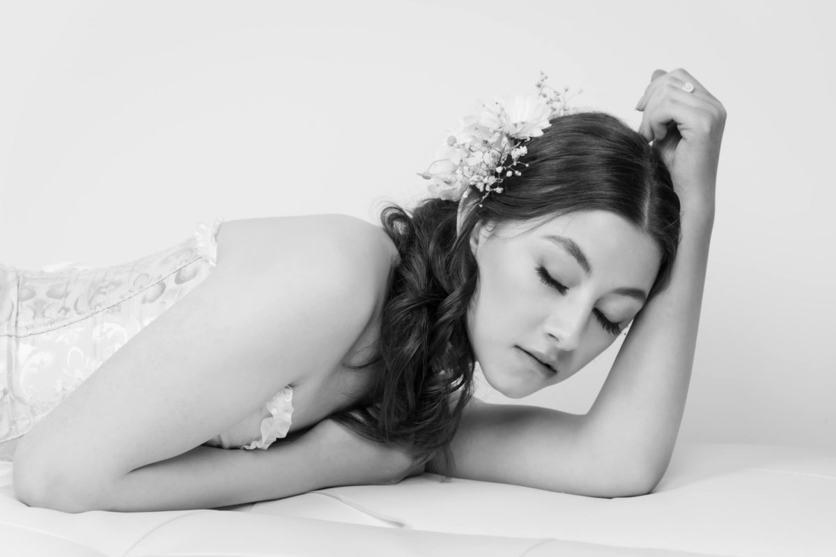 woman laying down with eyes closed with white background.