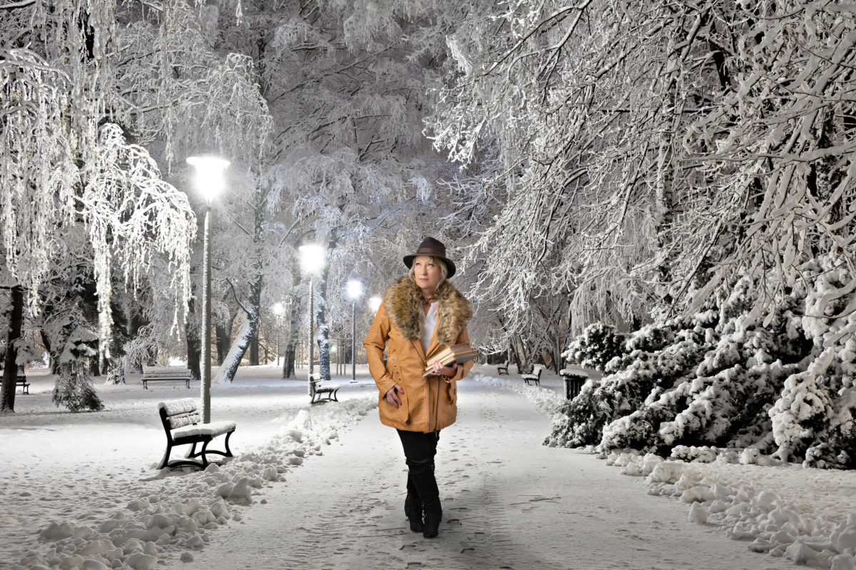 Woman holding books and standing on a snowy path in a park