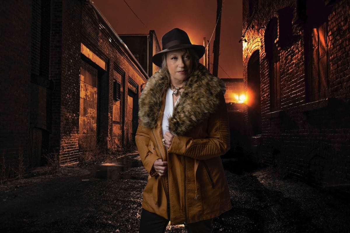 Woman alone in alley wearing a hat, fur collar jacket.