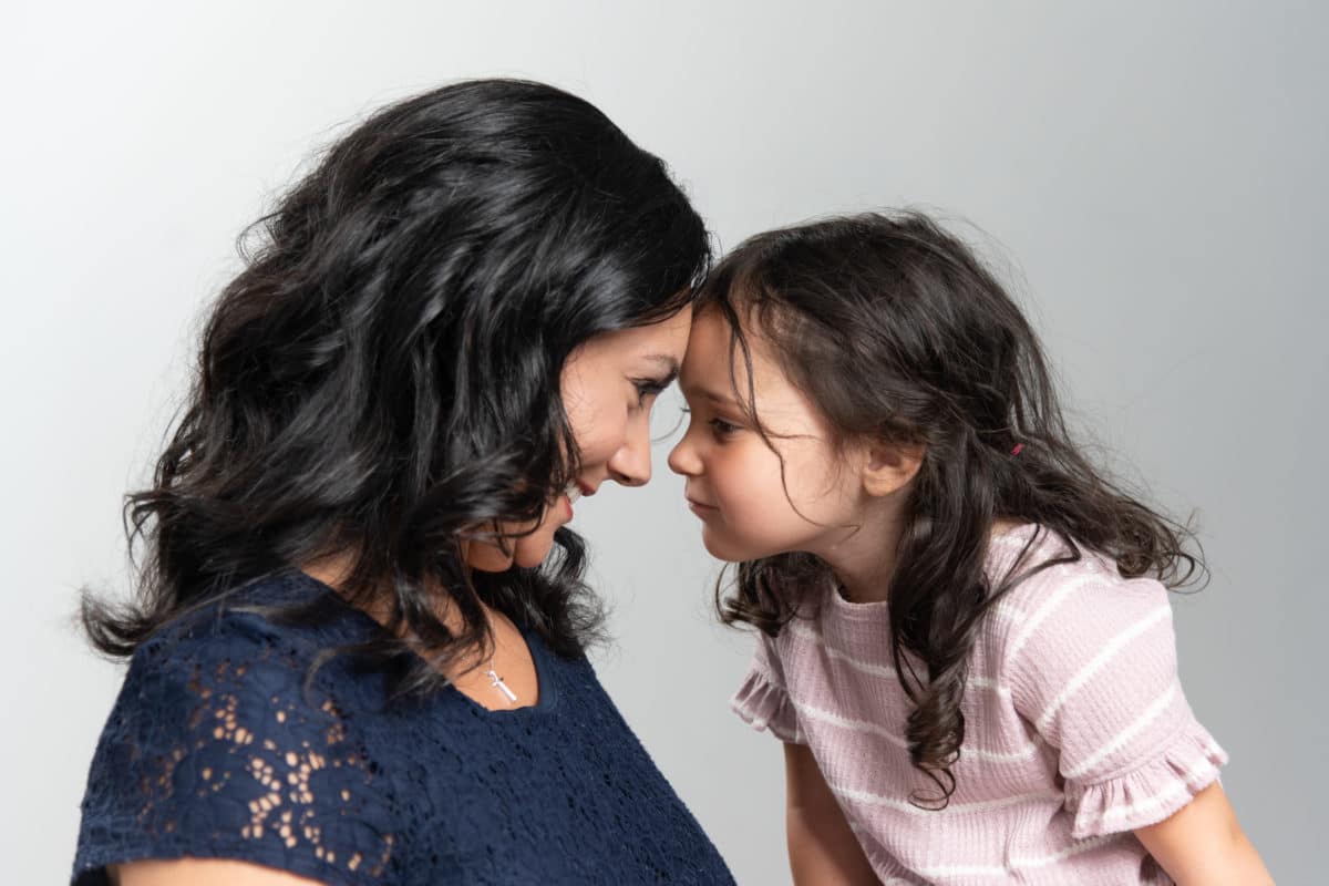 Portrait of a mother and daughter touching foreheads and staring into face while smiling.