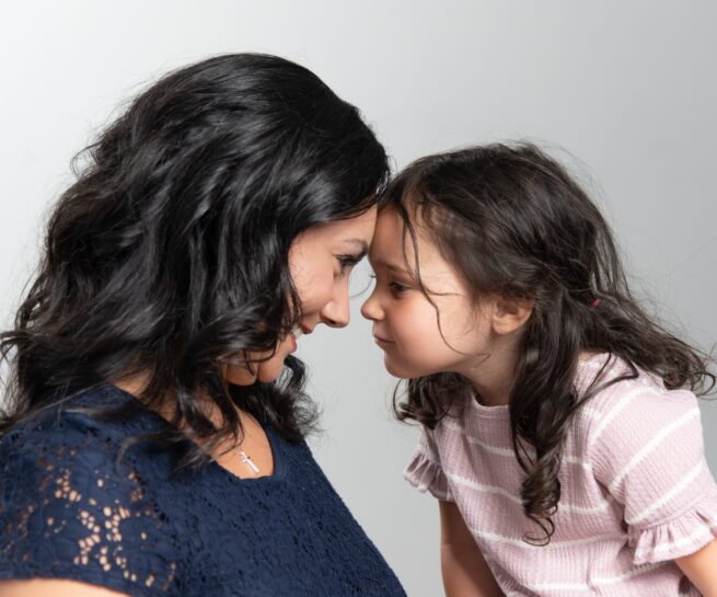 Portrait of a mother and daughter touching foreheads and staring into face while smiling.