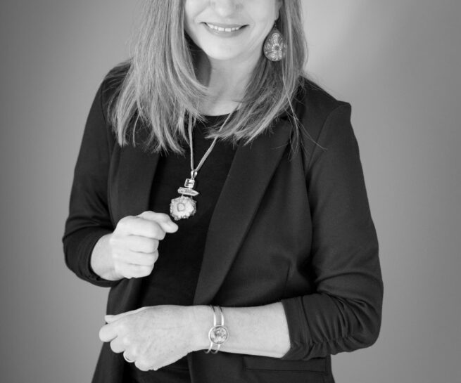 Portrait-Personal Branding photo of a woman in a suit jacket posing with her hands in slight fists as she smiles towards the camera.