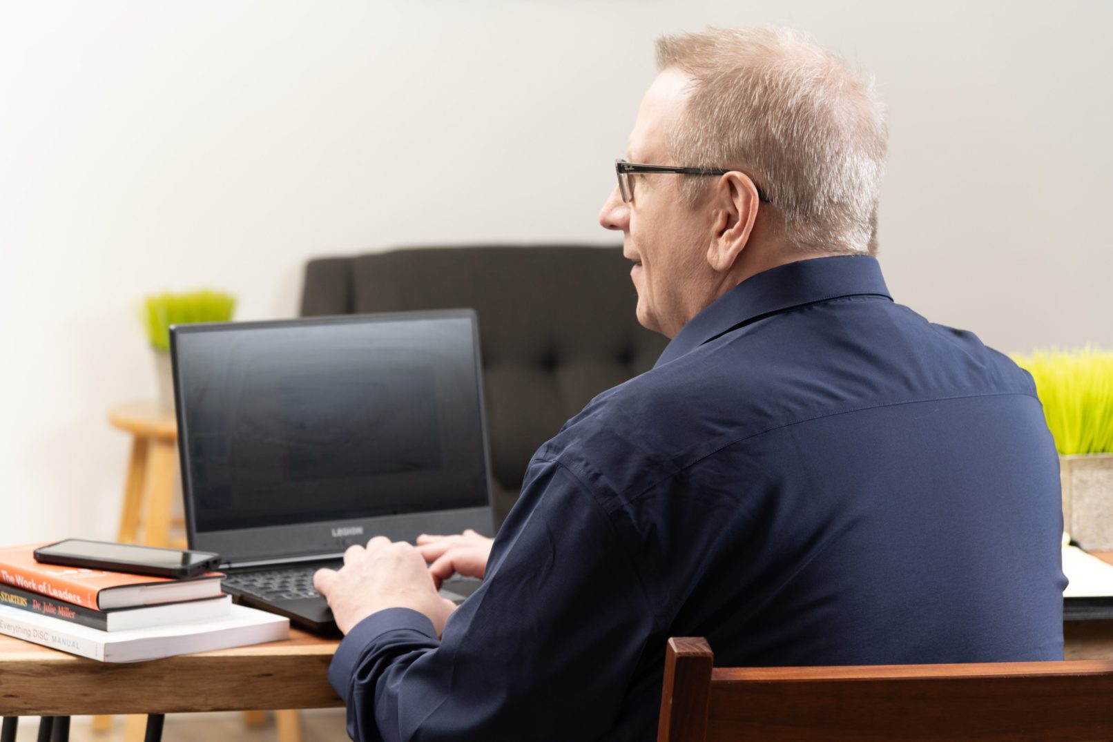 Portrait-Personal Branding photo of a man in a black fresh shirt sitting down and working on a black laptop at a desk.