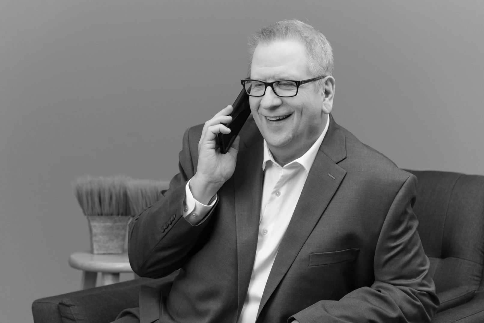 Portrait-Personal Branding photo of a man in glasses wearing a suit and talking on the cellphone in black and white.