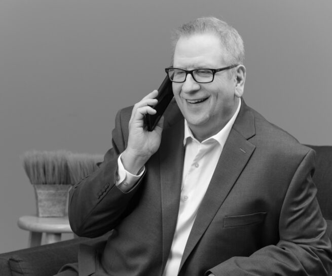 Portrait-Personal Branding photo of a man in glasses wearing a suit and talking on the cellphone in black and white.