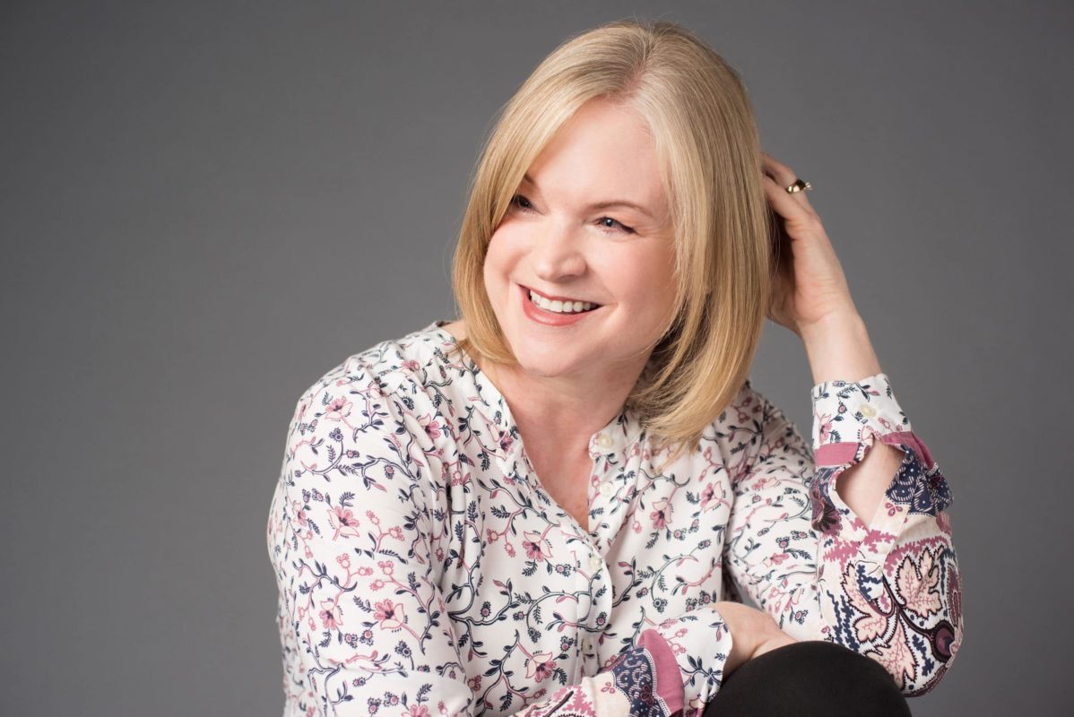 Portrait-Personal Branding photo of a woman smiling and looking off to the left with one hand behind her head and another on her leg.